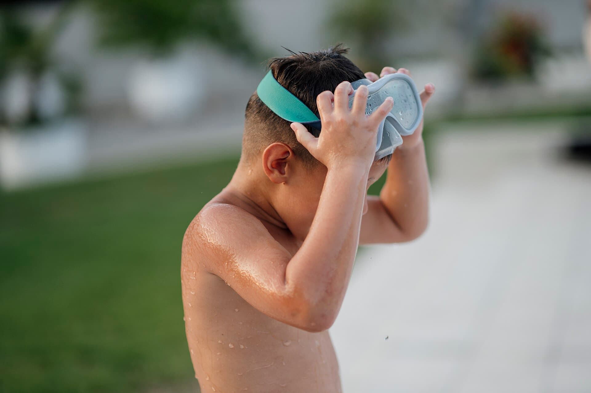 A child putting on swimming goggles beside a pool